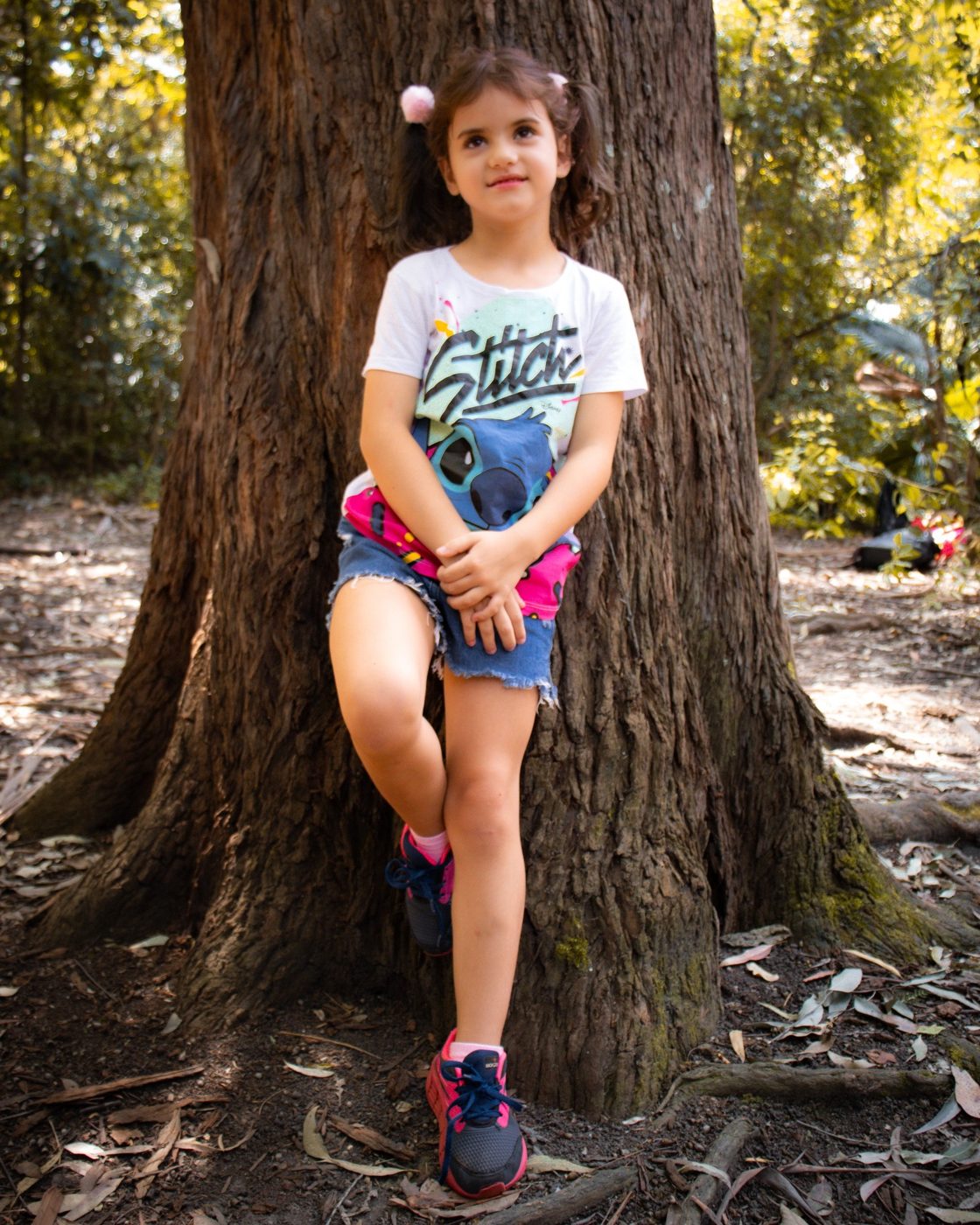 Menina encostada no tronco de uma árvore no parque