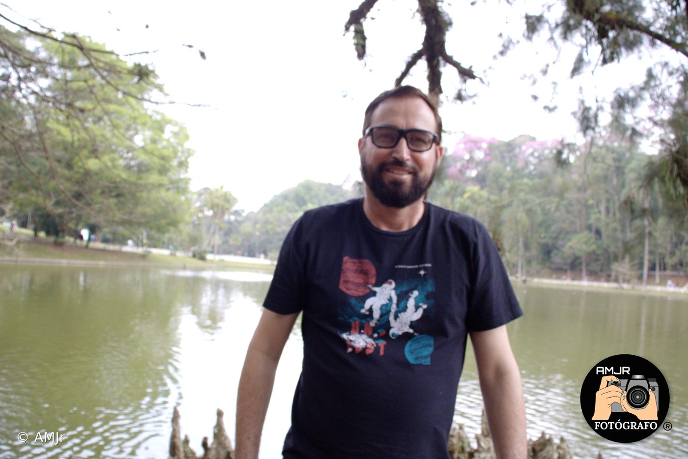 Homem de óculos sorrindo em frente ao lago do Horto