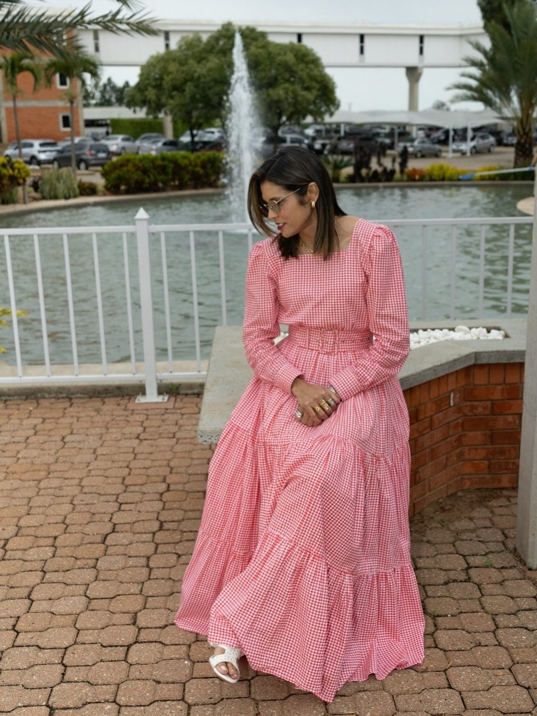 Mulher com vestido longo xadrez rosa em frente a chafariz